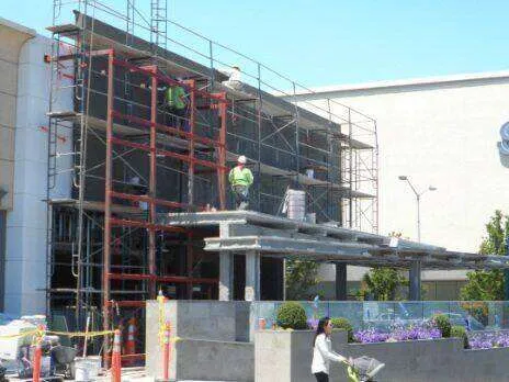 Scaffolding around a commercial building with workers, indicating ongoing construction or plaster work.