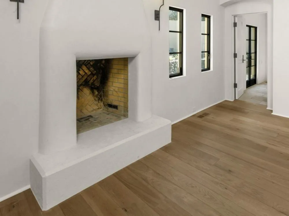 Interior view featuring a white stucco fireplace, wooden floors, and narrow black-framed windows.