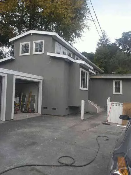 Gray stucco exterior of a residential home with garage and windows, surrounded by trees.
