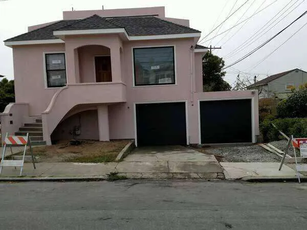 Residential home with pink stucco exterior and black garage doors, featuring a small porch.