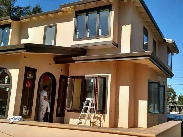 Two-story house with fresh stucco, worker near entrance, ladder against wall.