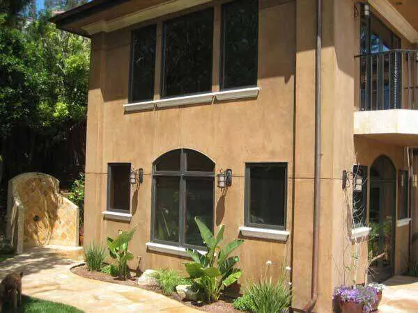Two-story house with smooth plaster finish, large windows, and landscaped garden.