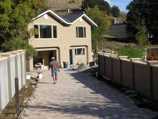 Two-story stucco home with paved driveway and construction materials around.