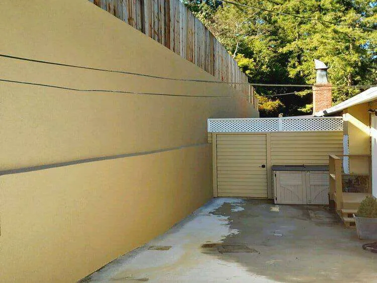 Smooth stucco retaining wall with wooden fence above, next to a driveway in Mill Valley.