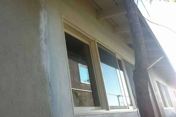 Close-up of a stucco wall with a visible patch around a window on a residential building exterior.