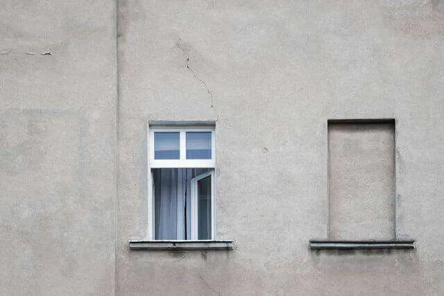 Stucco wall with visible cracks, an open window, and a sealed window space.